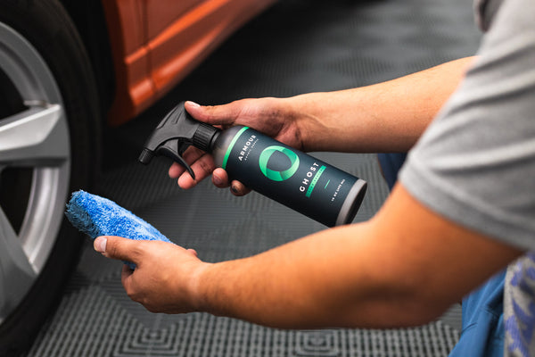 A person holding a spray bottle of Armour Detail Ghost and a blue applicator sponge.