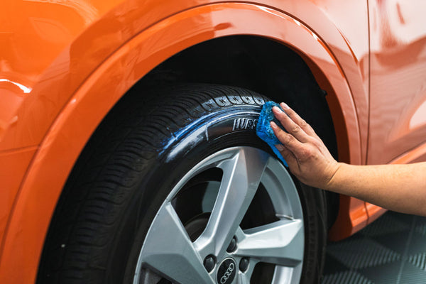 A person scrubbing a tire with a blue applicator sponge.