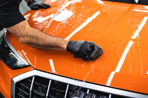 A closeup of a person washing an orange car with an Ultra Sponge.