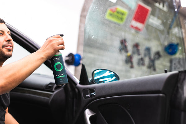 A person spraying the inside of a car window with a Armour Pilot.