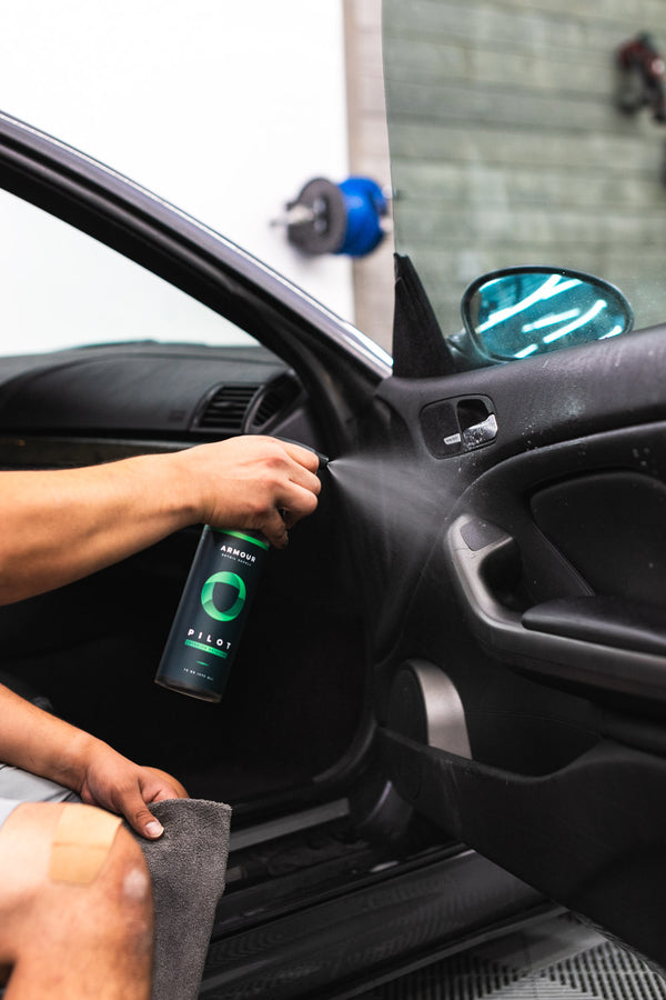 A closeup of a person spraying Pilot on the interior side of a car door.