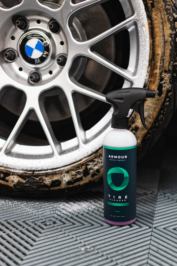 A spray bottle of Armour Tire Cleaner in front of a dirty tire.