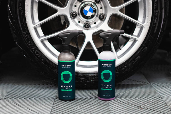 A spray bottle of Armour Wheel Cleaner and a spray bottle of Armour Tire Cleaner in front of a tire.