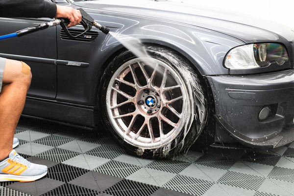 A closeup of a person power washing a car tire.