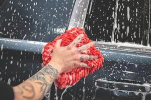 A person scrubbing a car door with a soaked red Chenille Knobby Mitt.