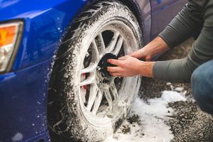 A blue car's tire covered in foam being wiped down by a black Edgeless towel.