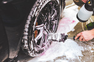 A person scrubbing a foamy tire with the Detail Factory Wheel brush.