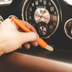 A hand brushing a car dash with an orange Detail Factory detailing brush.