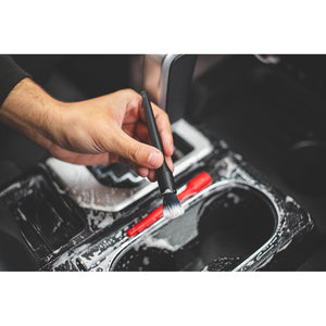 A person detailing the center console of a car with a black Detail Factory crevice brush.