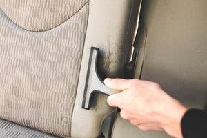 A gloved hand using a Detail Factory Pet Hair Rake on a vehicle seat.