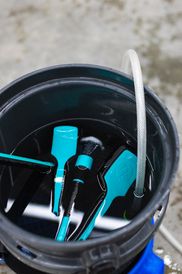 A Wheel Face Brush, Trigrip Brush, and Tire brush in a black bucket filled with water. 