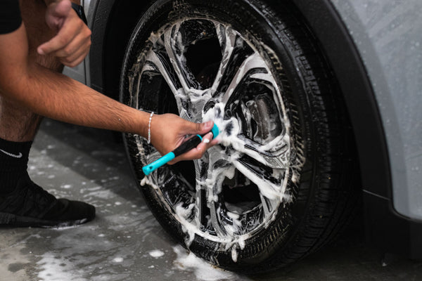 A person scrubbing a tire rim with the Riptide Trigrip brush.