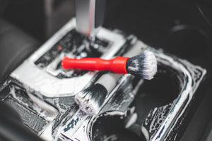 A red and grey Detail Factory Ultra soft short brushes covering each other on a center console with foam all over it.