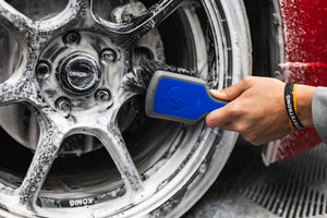 A person using a Detail Factory Wheel Face Brush Avalanche to clean a red vehicle's tire.