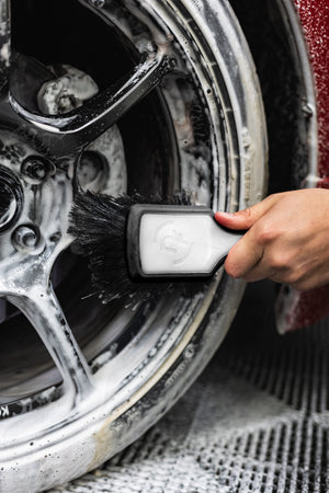 A person using a Detail Factory Wheel Face Brush Black Ice to clean a red vehicle's tire.