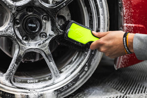 A person using a Detail Factory Wheel Face Brush Ectoplasm to clean a red vehicle's tire.