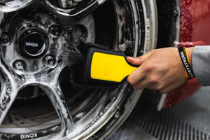 A person using a Detail Factory Wheel Face Brush Livewire to clean a red vehicle's tire.