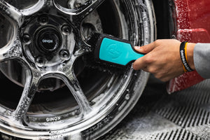 A person using a Detail Factory Wheel Face Brush Riptide to clean a red vehicle's tire.