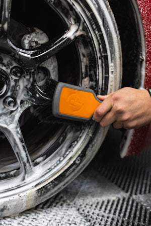 A person using a Detail Factory Wheel Face Brush Solar Flare to clean a red vehicle's tire.