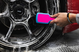 A person using a Detail Factory Wheel Face Brush Underglow to clean a red vehicle's tire.
