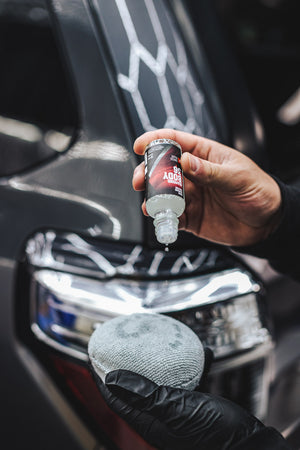 A person pouring Diamond Protech Body 36 onto a pearl puck applicator with a background of  grey suv.