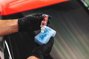 A close up of a person wearing black rubber gloves pouring Diamon Protech Diamond Glass onto a blue sponge.