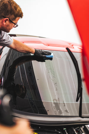 A person washing a car window with a blue sponge.