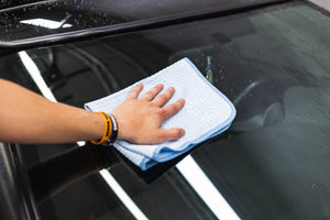 Person cleaning a car window with a light blue 16x24 dry me a river microfiber towel.