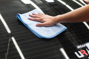 Person cleaning a car window with a light blue 16x24 dry me a river microfiber towel.