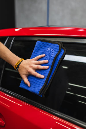 Person cleaning a car window with a navy blue 16x24 dry me a river microfiber towel.