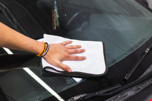 Person cleaning a car window with a white 16x24 dry me a river microfiber towel.