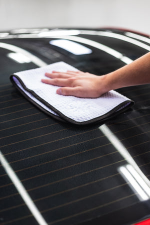 Person cleaning a car window with a white 16x24 dry me a river microfiber towel.
