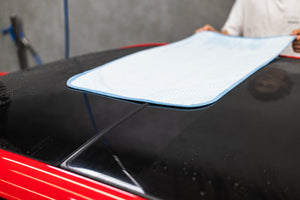 Person cleaning a car sunroof with a light blue 20x40 dry me a river microfiber towel.