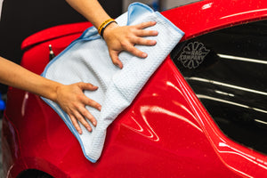 Person cleaning a car with a light blue 20x40 dry me a river microfiber towel.