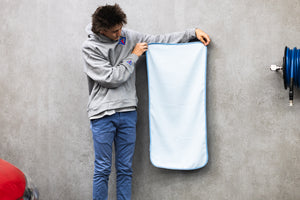 Person holding a light blue 20x40 dry me a river microfiber towel next to a red car.