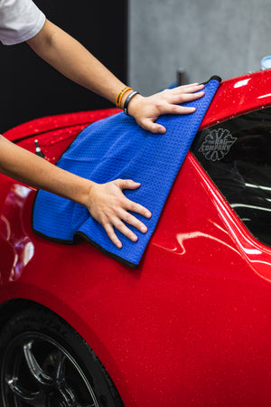 Person cleaning a car with a navy blue 20x40 dry me a river microfiber towel.