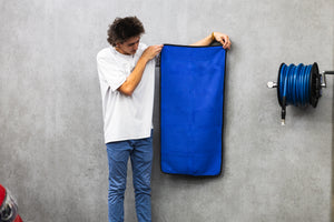 Person holding a navy blue 20x40 dry me a river microfiber towel next to a red car.