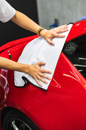 Person cleaning a car with a white 20x40 dry me a river microfiber towel.