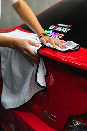 Person cleaning a car with a white 26x59 dry me a river microfiber towel.
