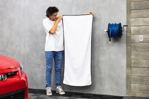 Person holding a white 26x59 dry me a river microfiber towel next to a red car.