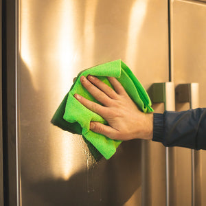 A person cleaning a stainless steal fridge door with a green edgless towel.