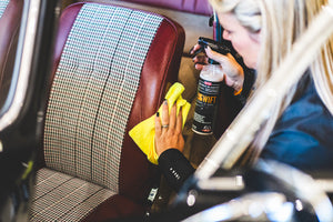 Person cleaning a car seat with a yellow microfiber towel and a spray bottle of P&S Swift