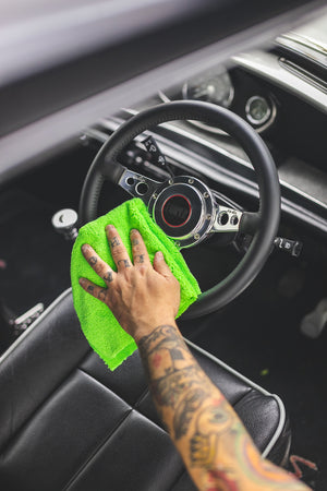 A hand scrubbing a car steering wheel with a lime green Edgeless towel.