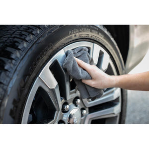 A person scrubbing a tire rim with a grey Edgeless towel.