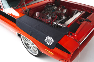 An open engine bay of a red classic car with a black fender cover displaying 'The Rag Company' logo draped over the side.