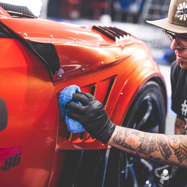 A person scrubbing Gtechniq halo onto an orange Toyota gt86 with a blue sponge.