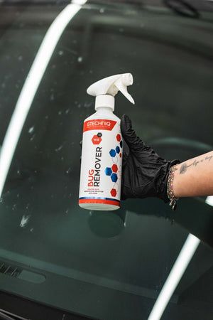 Hand holding a bottle of Gtechniq Bug Remover in front of a car window.