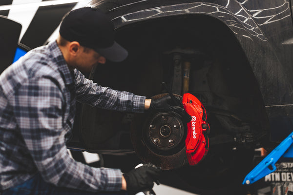 A person scrubbing a brake pad with a black Detail Factory Brush.