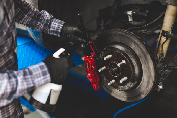 Person using an IK Multi TR Mini 360 Trigger Sprayer to apply cleaner to a brake pad while scrubbing it with a black Detail Factory Brush.