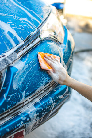 A person scrubbing a foamy blue car with an orange jersey bug scrubber.